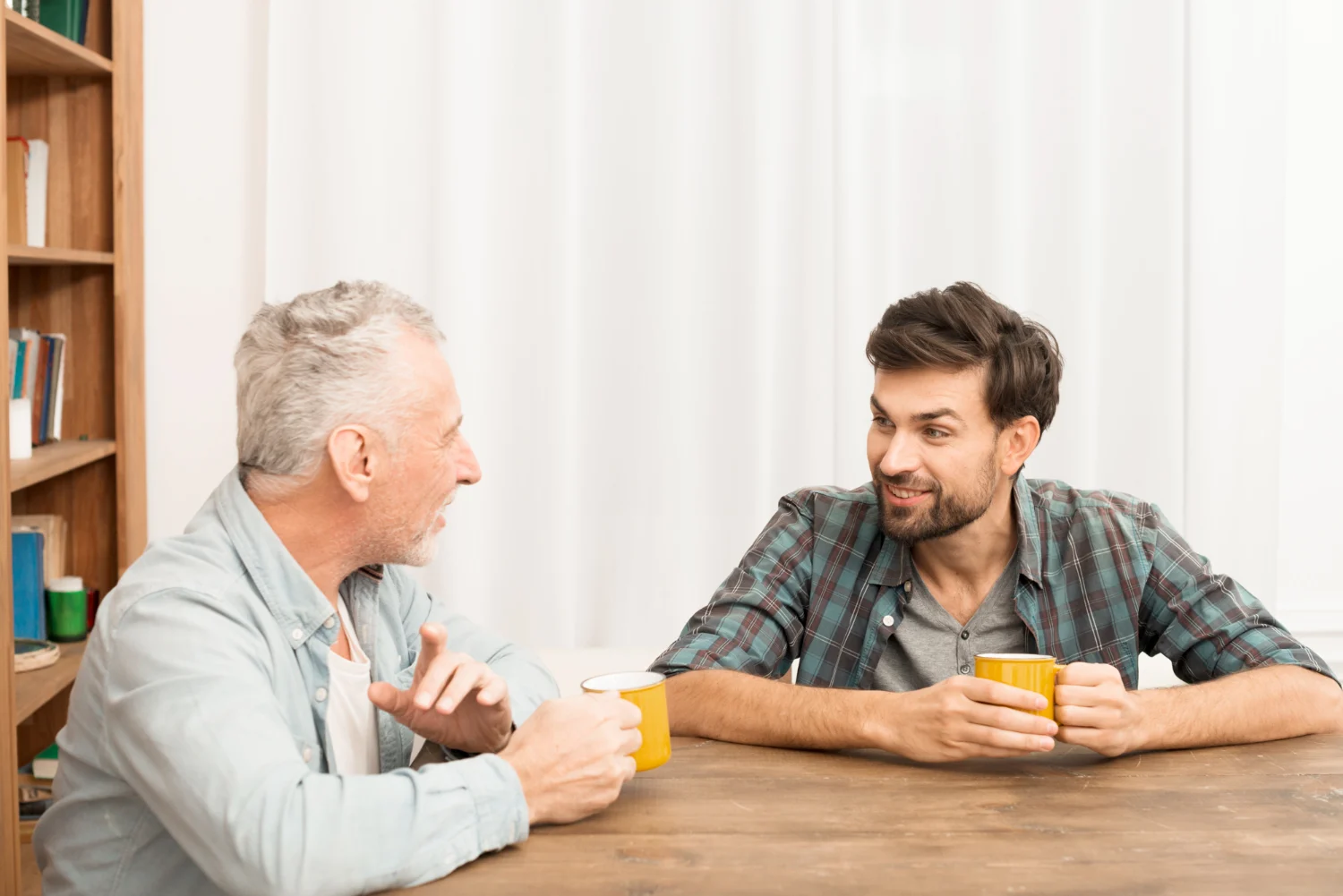 Young man and middle aged man smiling with mugs at table