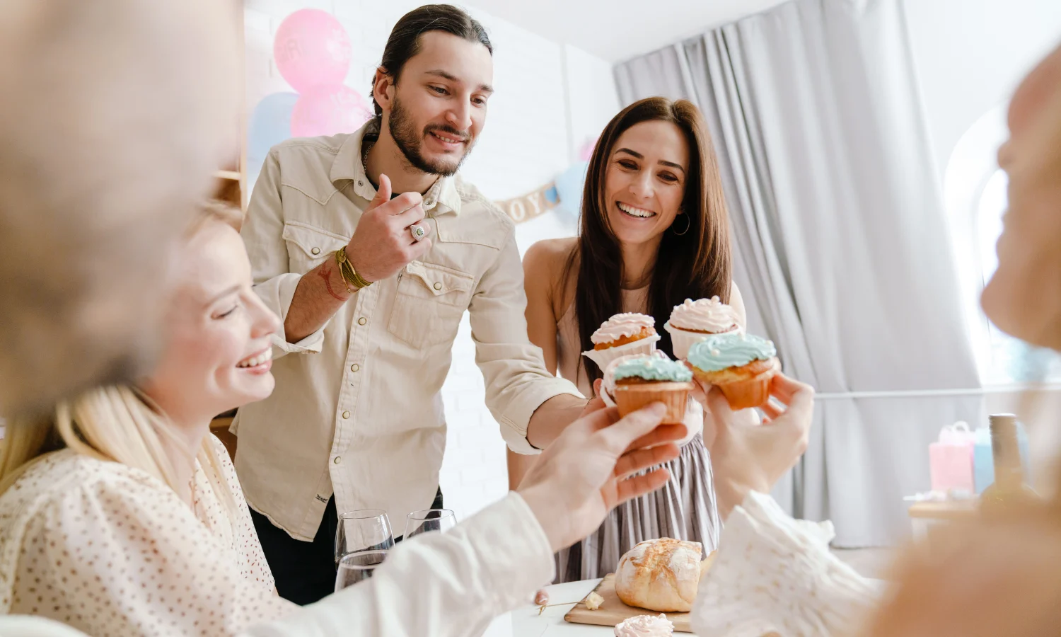 Couple and friends celebrating at a gender reveal party eating cupcakes